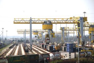 Pátio logístico com contêineres e movimentação de carga em recinto alfandegado.